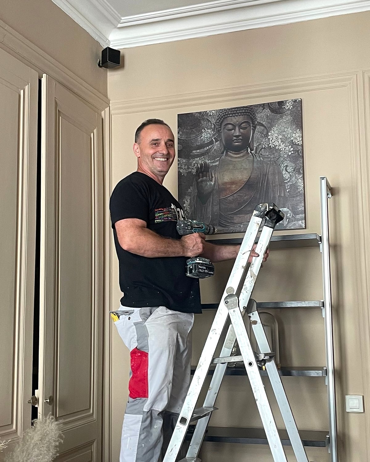 Le fondateur de BTI FINITION, souriant sur son escabeau, perceuse en main, pendant un chantier